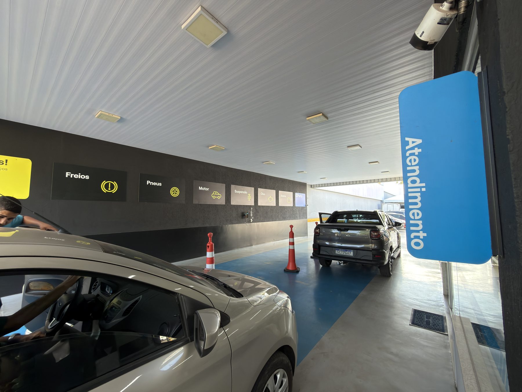 Placa de atendimento na entrada do box, com o painel de serviços da rede Porto ao fundo