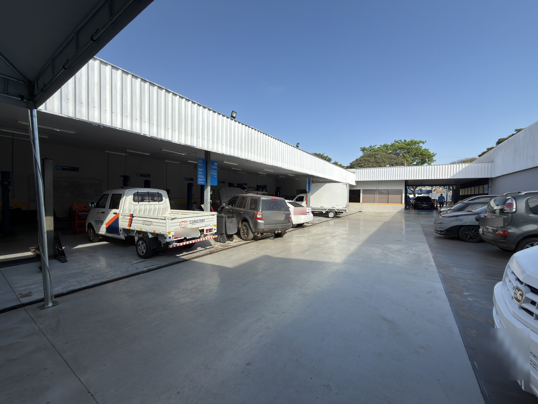 Pátio coberto da oficina com vários carros e o galpão de serviço ao fundo